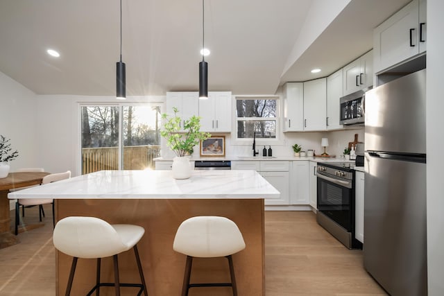 kitchen featuring light stone counters, a center island, stainless steel appliances, a kitchen bar, and a sink