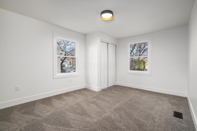 unfurnished bedroom featuring baseboards, multiple windows, visible vents, and dark carpet