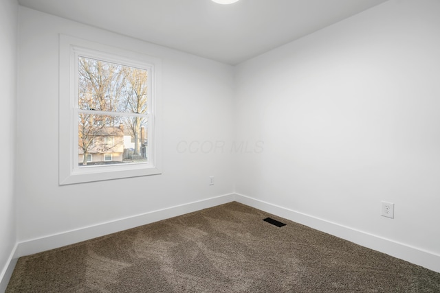 spare room featuring dark colored carpet, visible vents, and baseboards