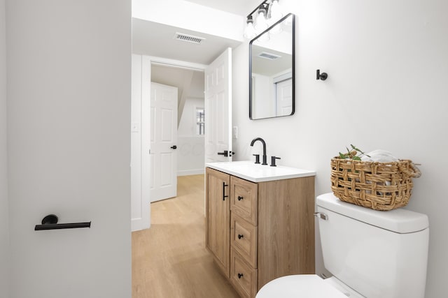 half bath featuring toilet, visible vents, wood finished floors, and vanity