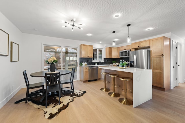 kitchen featuring light countertops, appliances with stainless steel finishes, light wood-type flooring, and backsplash