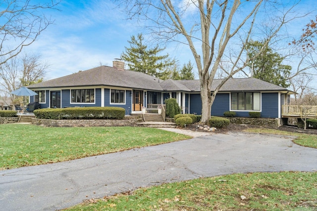 ranch-style home featuring a front yard, roof with shingles, driveway, and a chimney