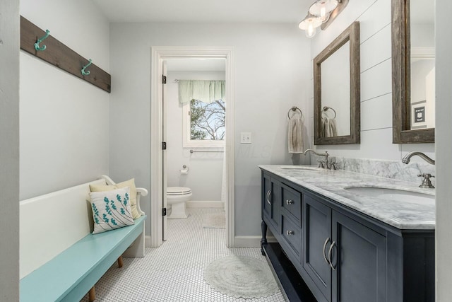 bathroom with a sink, baseboards, toilet, and double vanity