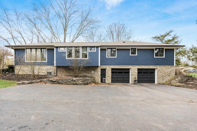 view of front of property featuring an attached garage, central AC unit, stone siding, and driveway