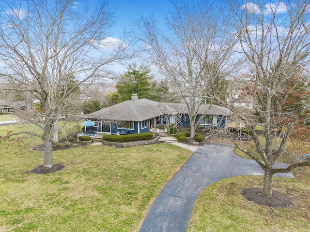 view of front facade with driveway, a chimney, and a front lawn