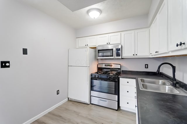 kitchen featuring a sink, white cabinetry, appliances with stainless steel finishes, light wood-type flooring, and dark countertops