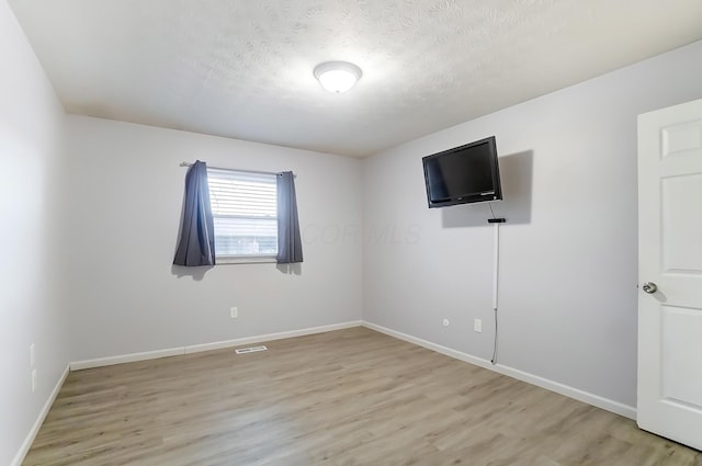 unfurnished bedroom featuring a textured ceiling, baseboards, visible vents, and light wood-style floors