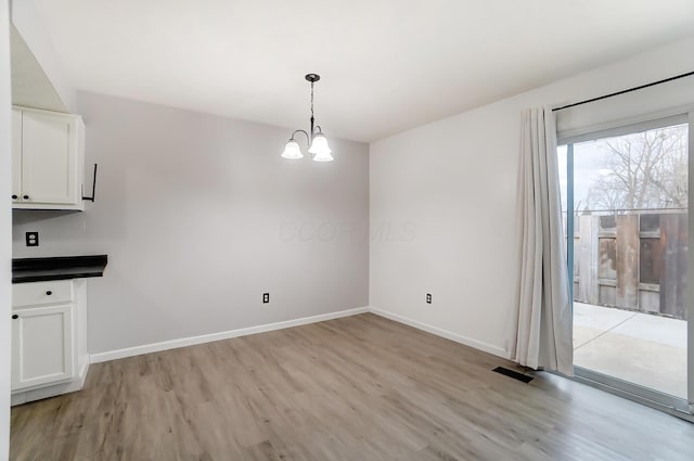 unfurnished dining area featuring light wood-style floors, visible vents, a notable chandelier, and baseboards