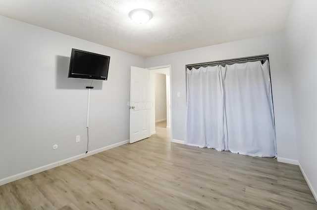 unfurnished bedroom featuring baseboards, a textured ceiling, and light wood-style floors