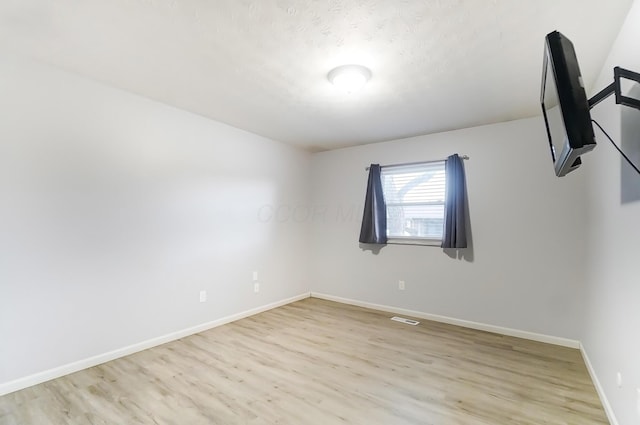 empty room with light wood-style floors, visible vents, and baseboards