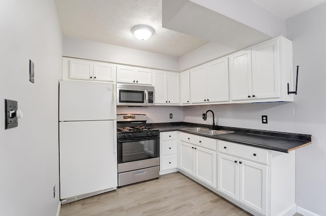 kitchen featuring dark countertops, light wood-style flooring, appliances with stainless steel finishes, and a sink