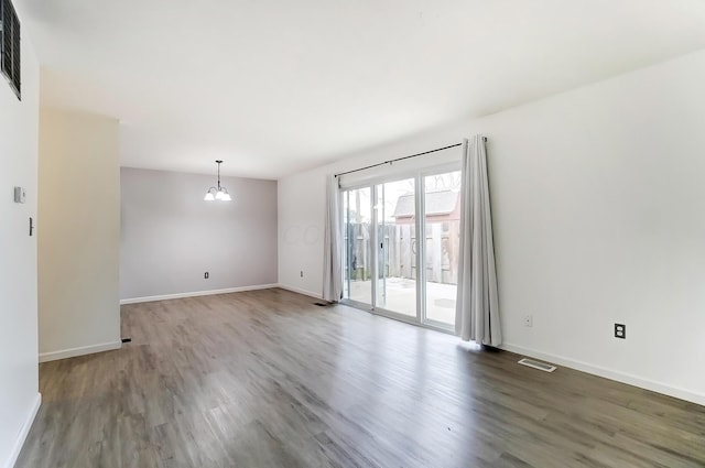 unfurnished room with baseboards, visible vents, a chandelier, and wood finished floors