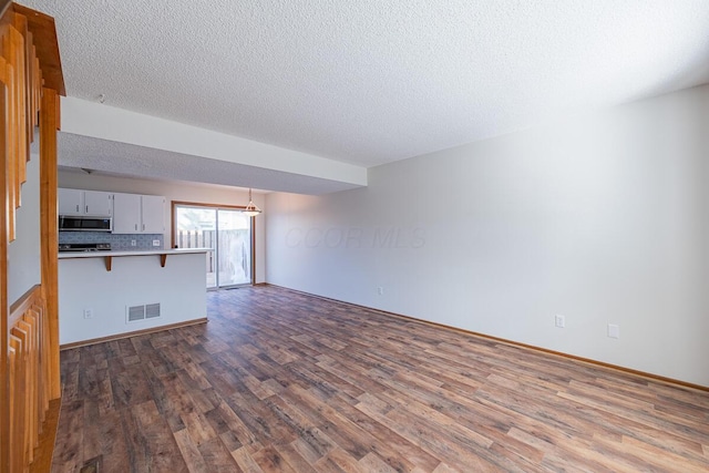 unfurnished living room featuring dark wood-style floors, visible vents, and a textured ceiling