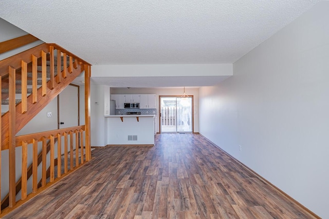 unfurnished living room featuring a textured ceiling, dark wood-style flooring, stairway, and visible vents