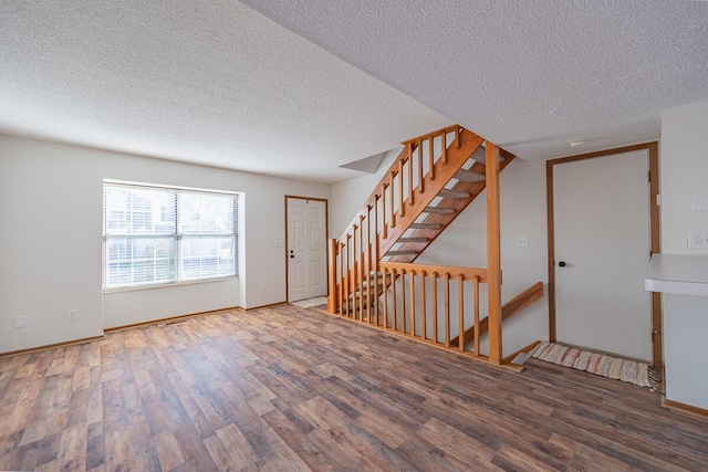 spare room featuring a textured ceiling, stairway, wood finished floors, and baseboards