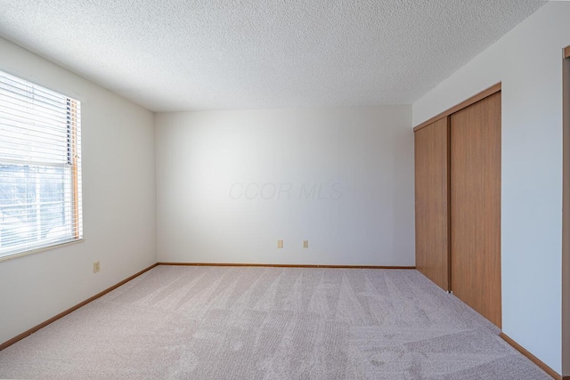 unfurnished bedroom with a closet, light carpet, a textured ceiling, and baseboards