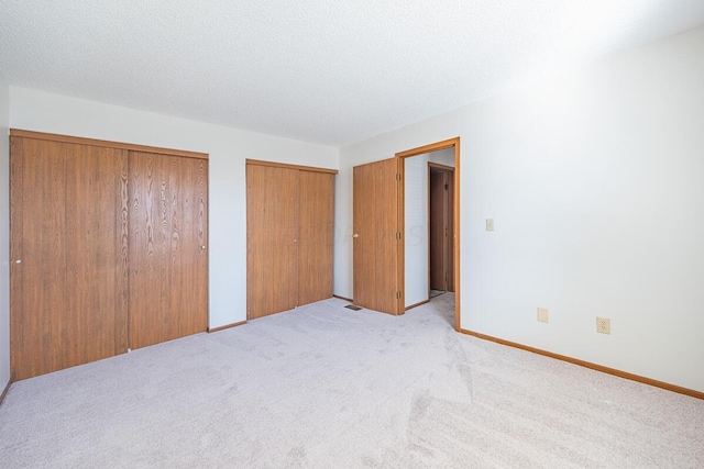 unfurnished bedroom with multiple closets, light colored carpet, a textured ceiling, and baseboards