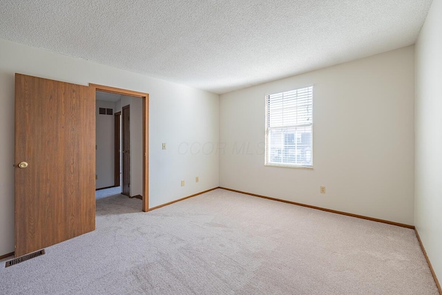 carpeted spare room with a textured ceiling, visible vents, and baseboards