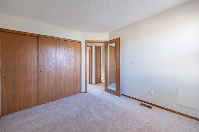 unfurnished bedroom featuring a textured ceiling, carpet flooring, visible vents, baseboards, and a closet