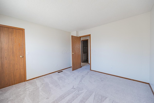 empty room with carpet, visible vents, a textured ceiling, and baseboards