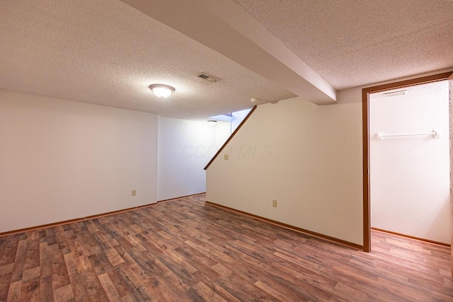 finished below grade area with stairway, a textured ceiling, visible vents, and wood finished floors