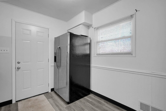 kitchen featuring light wood-style flooring, a wainscoted wall, visible vents, white cabinetry, and stainless steel fridge