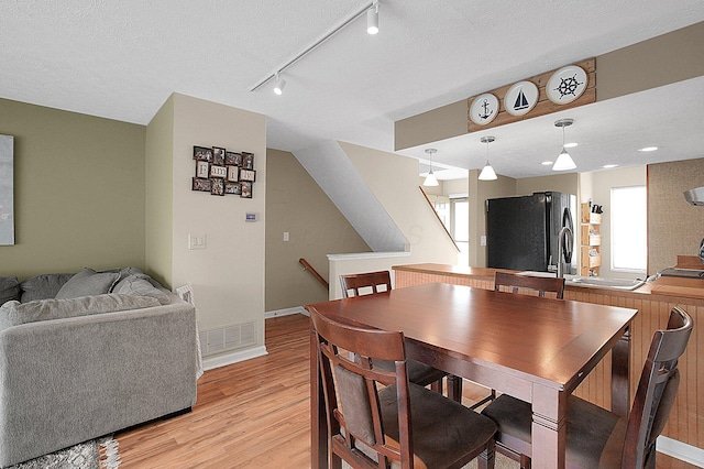 dining room featuring plenty of natural light, light wood-style flooring, visible vents, and a textured ceiling