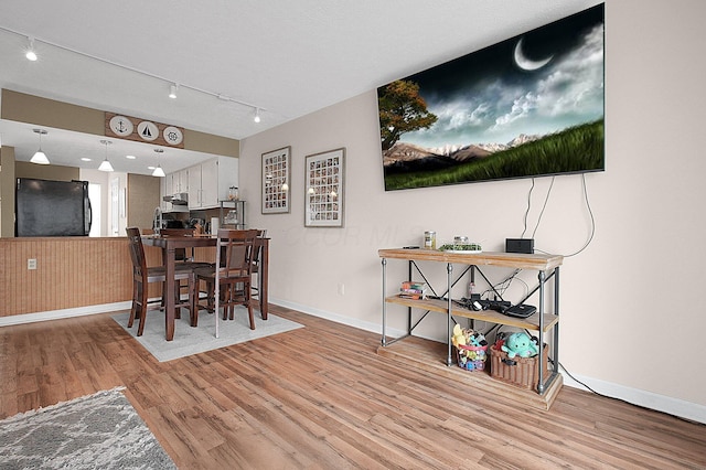 dining space featuring wood finished floors, rail lighting, and baseboards