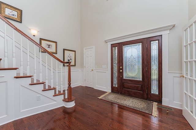 foyer entrance with a decorative wall, a high ceiling, wainscoting, wood finished floors, and stairs