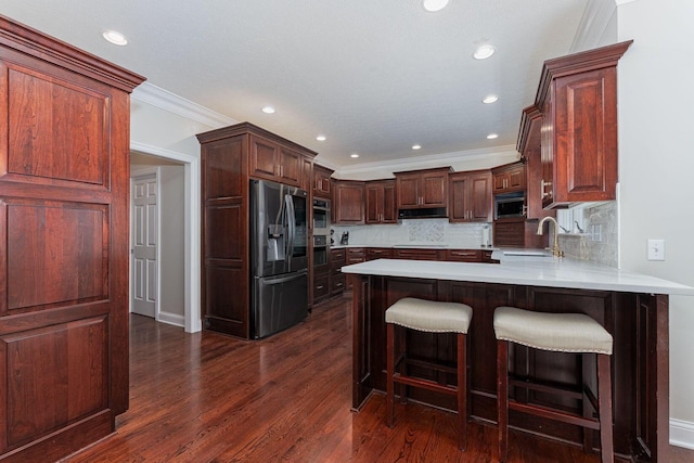 kitchen featuring dark wood-style floors, stainless steel appliances, light countertops, a sink, and a peninsula