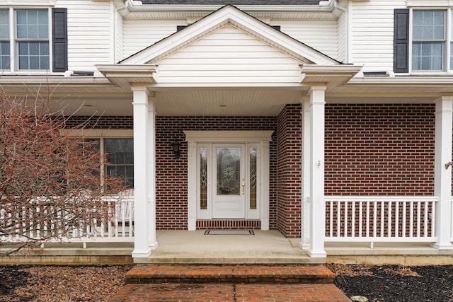 doorway to property featuring brick siding and a porch