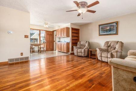 living room featuring visible vents, ceiling fan, and wood finished floors