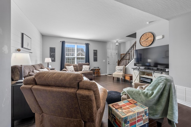 living room featuring a textured ceiling, wood finished floors, visible vents, baseboards, and stairs