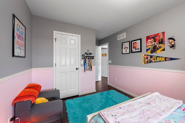 bedroom featuring baseboards, visible vents, a textured ceiling, and wood finished floors