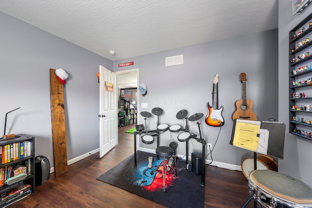 exercise room featuring baseboards, a textured ceiling, visible vents, and wood finished floors