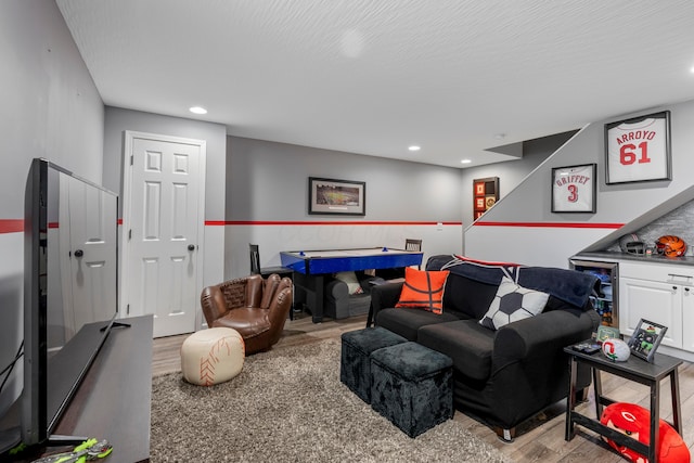 living room with a bar, a wainscoted wall, wine cooler, a textured ceiling, and light wood-type flooring