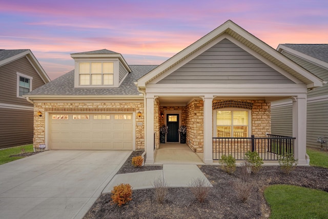 view of front of home featuring an attached garage, covered porch, a shingled roof, driveway, and stone siding