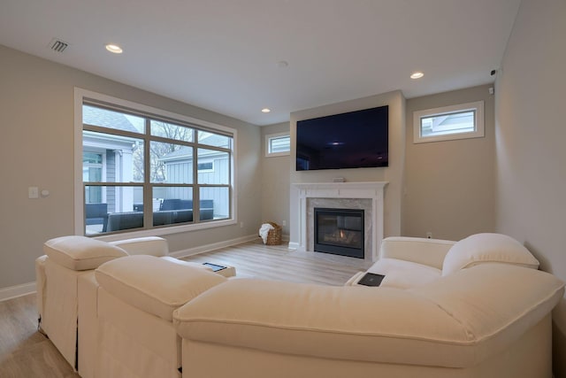 living area featuring baseboards, a healthy amount of sunlight, a fireplace, and light wood finished floors