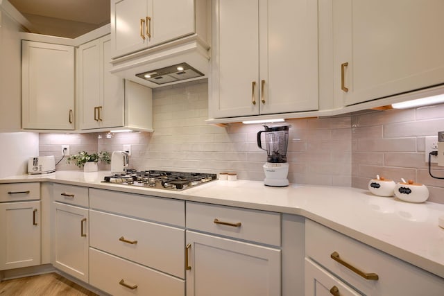 kitchen with under cabinet range hood, light countertops, stainless steel gas stovetop, and backsplash