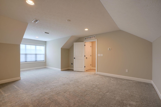 additional living space featuring light carpet, visible vents, and a textured ceiling