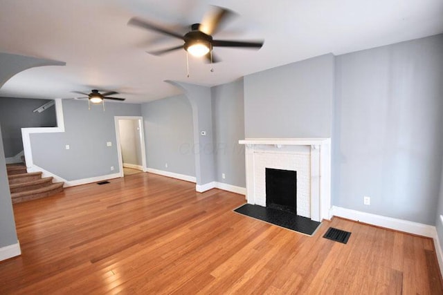 unfurnished living room featuring arched walkways, a fireplace, wood finished floors, baseboards, and stairs