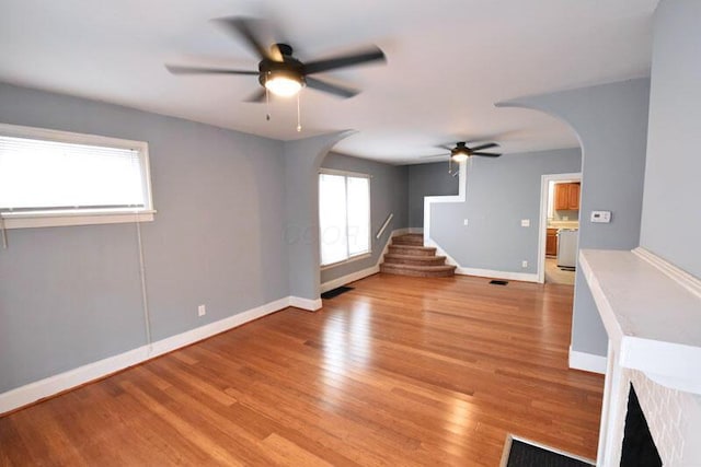 unfurnished living room with light wood-type flooring, stairway, plenty of natural light, and arched walkways