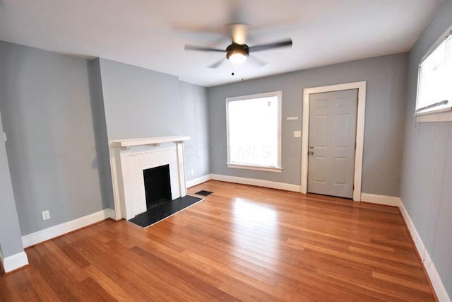 unfurnished living room with light wood finished floors, a brick fireplace, and baseboards