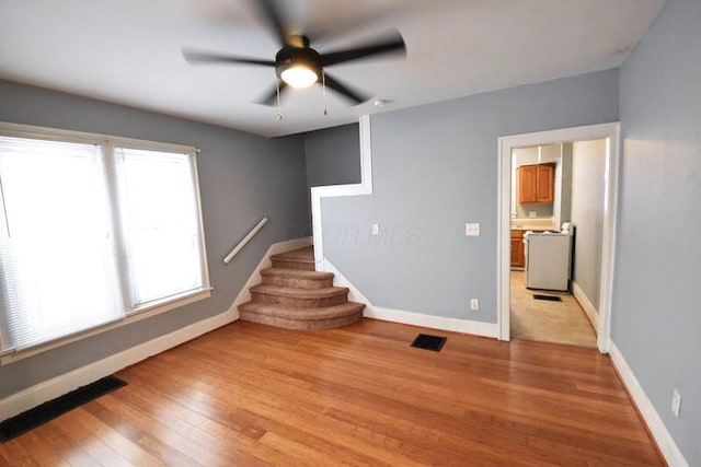 spare room featuring a ceiling fan, visible vents, baseboards, stairway, and light wood-type flooring