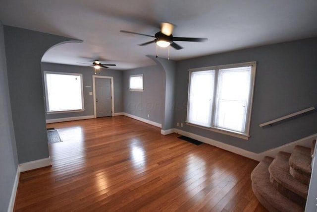 unfurnished living room featuring arched walkways, hardwood / wood-style flooring, baseboards, and stairs