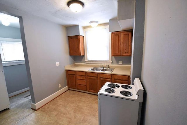 kitchen with white appliances, a sink, baseboards, light countertops, and brown cabinets