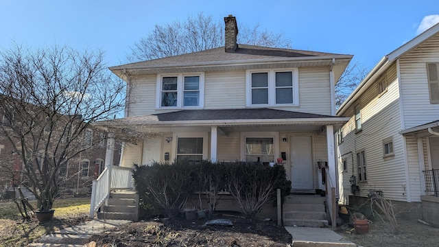 american foursquare style home with a porch, roof with shingles, and a chimney