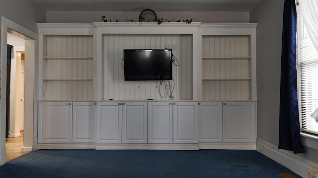 unfurnished living room featuring baseboards and dark colored carpet