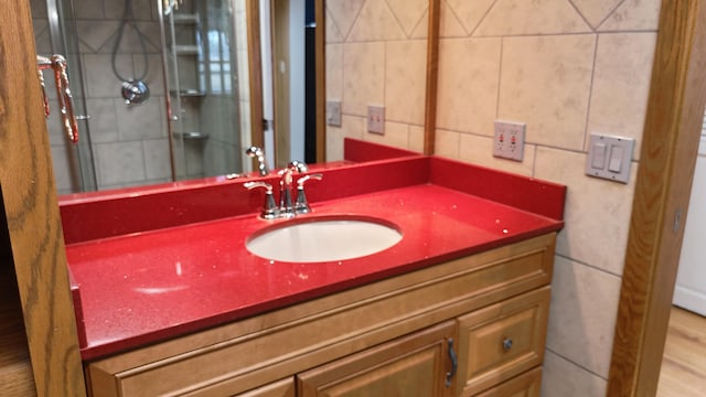 bathroom with a shower with door, tile walls, and vanity