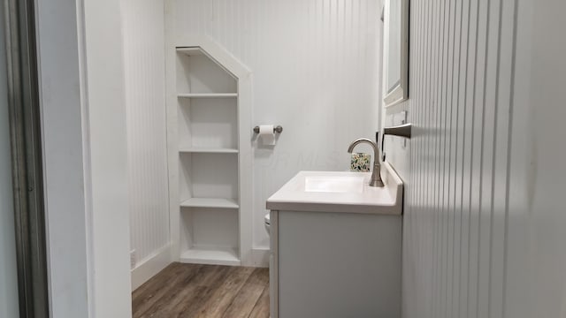 bathroom with built in features, toilet, vanity, and wood finished floors